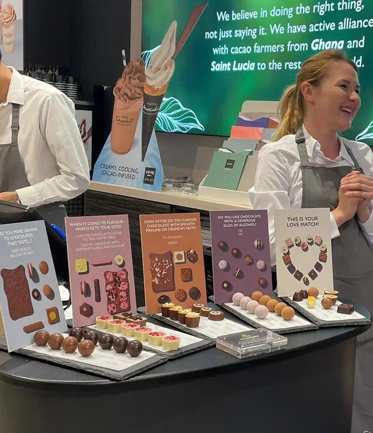 a man and woman standing behind a counter with a display of chocolate