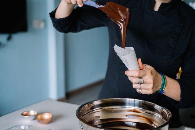 Chef-spooning-melted-chocolate-into-a-white-piping-bag-over-a-silver-bowl