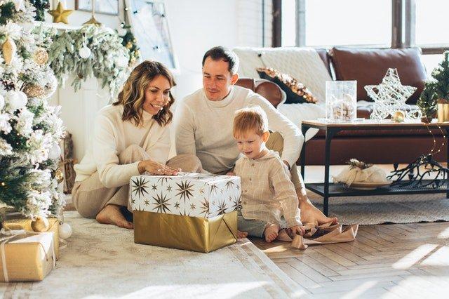Parents-and-child-opening-wrapped-present-by-a-Christmas-tree