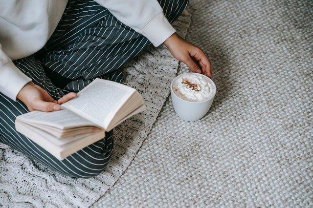 Person-with-book-holding-mug-of-hot-chocolate-with-whipped-cream