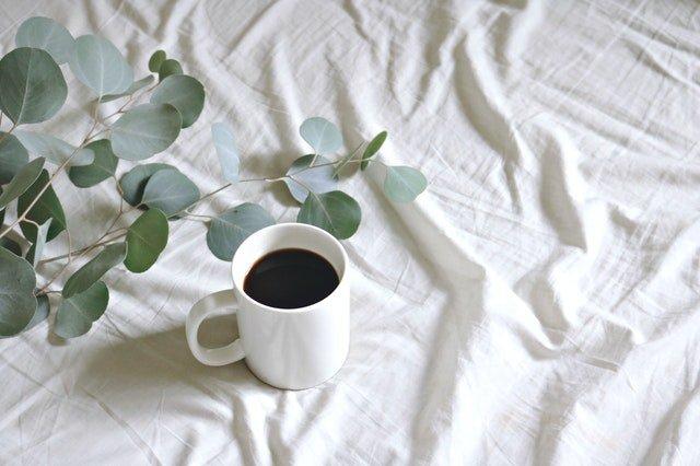 White-coffee-mug-on-white-bedsheets-with-foliage