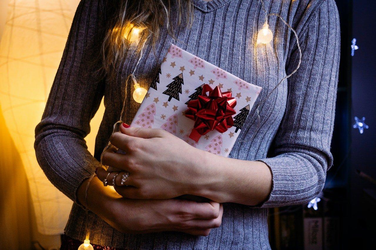 Woman-holding-Christmas-gift-wrapped-in-white-paper