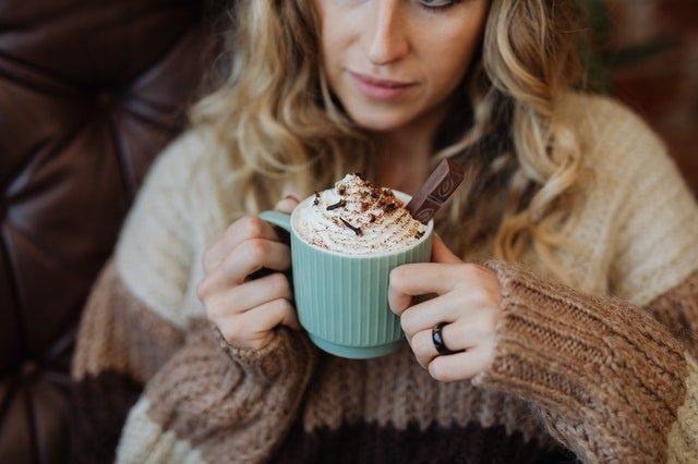Woman-in-brown-jumper-drinking-cream-topped-hot-chocolate-in-a-blue-mug
